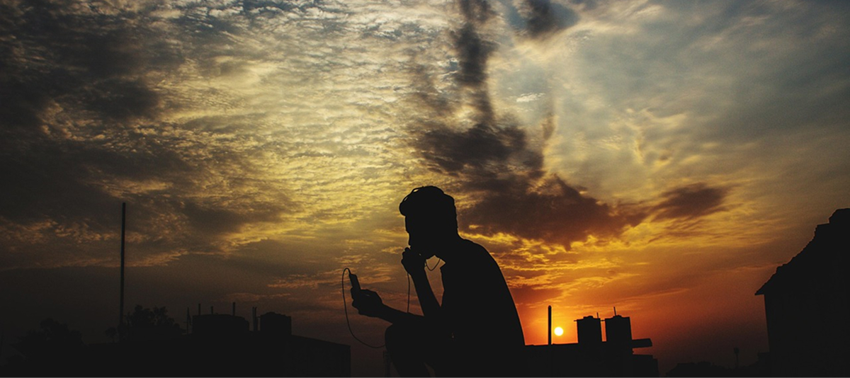 Silhouette of a man holding a cell phone against a vibrant sunset backdrop.