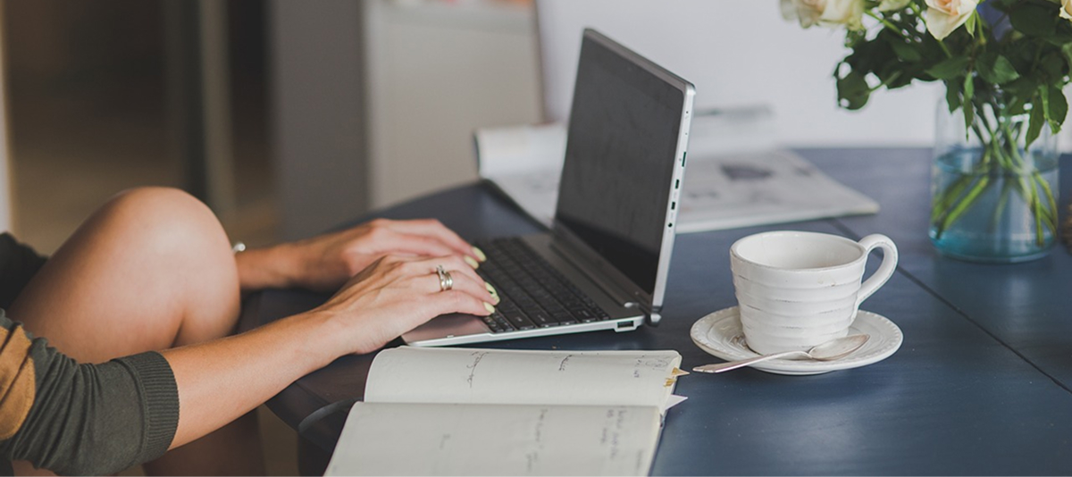 A woman types on her laptop at a table, focused on her work in a well-lit environment.