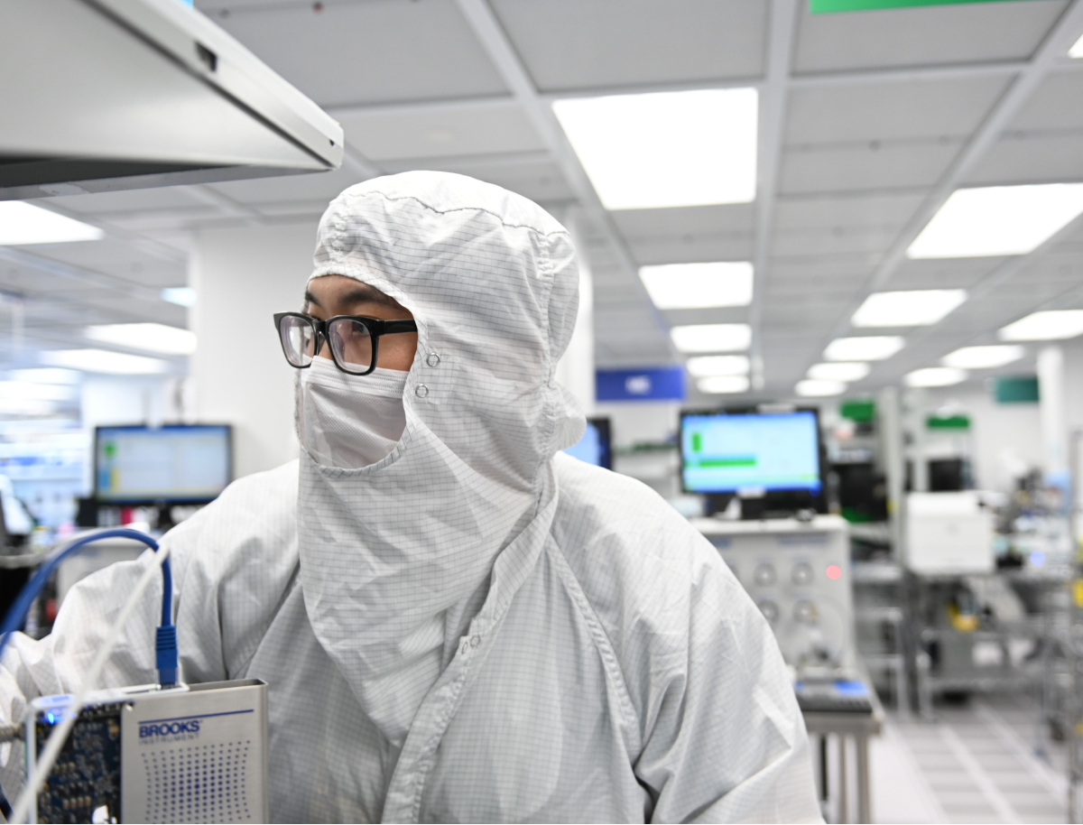 A Brooks Instrument employee wearing a white lab coat stands in a laboratory setting.