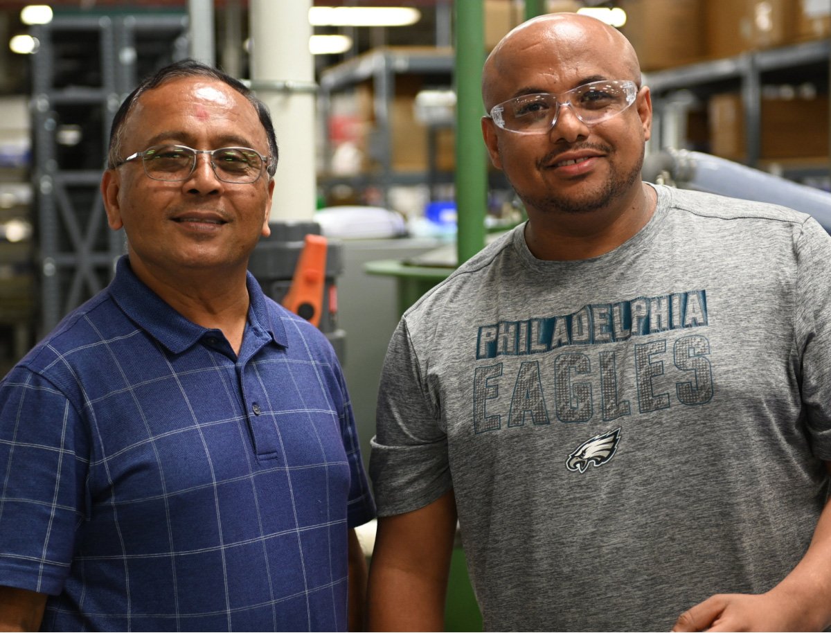 Two men in a warehouse, standing near shelves stocked with boxes and equipment.