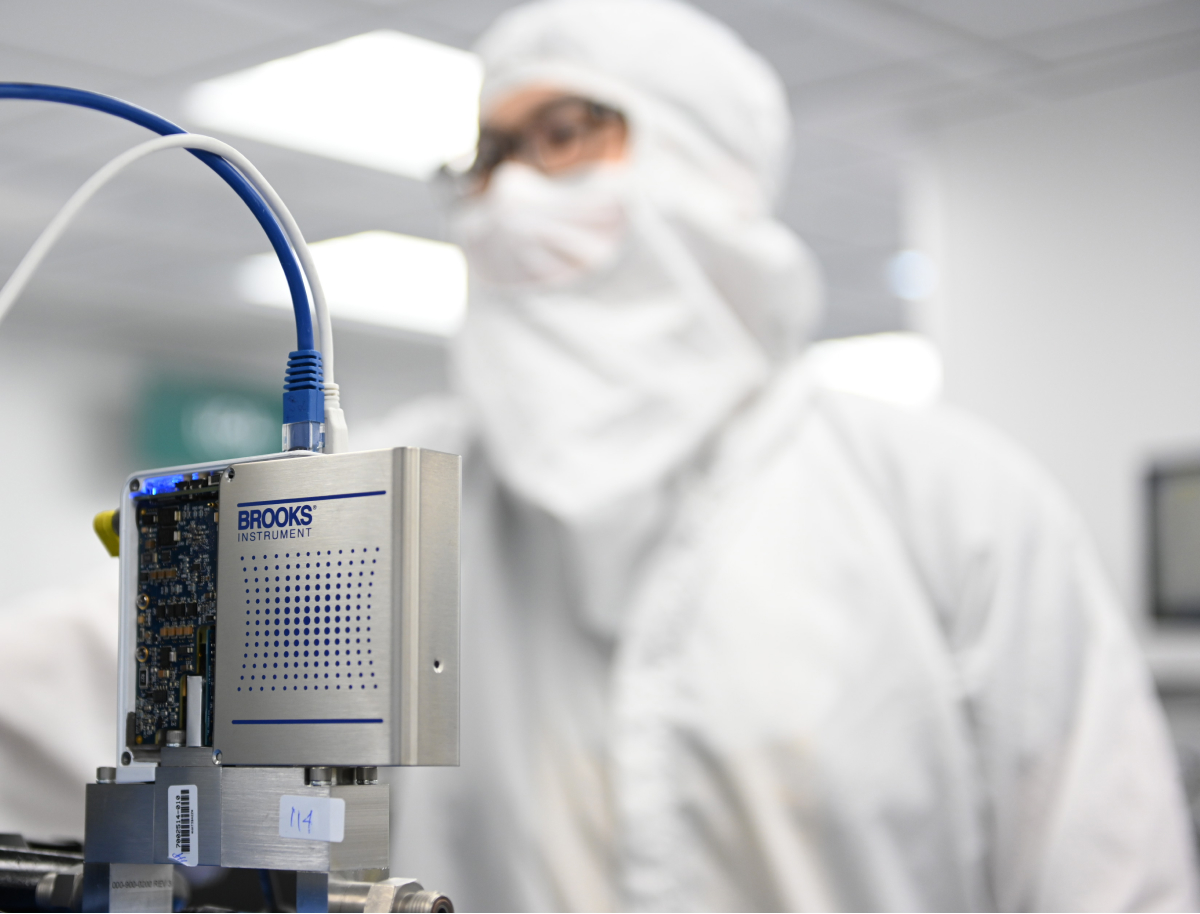 A Brooks Instrument employee in a lab coat holds a device, showcasing their work in a laboratory setting.