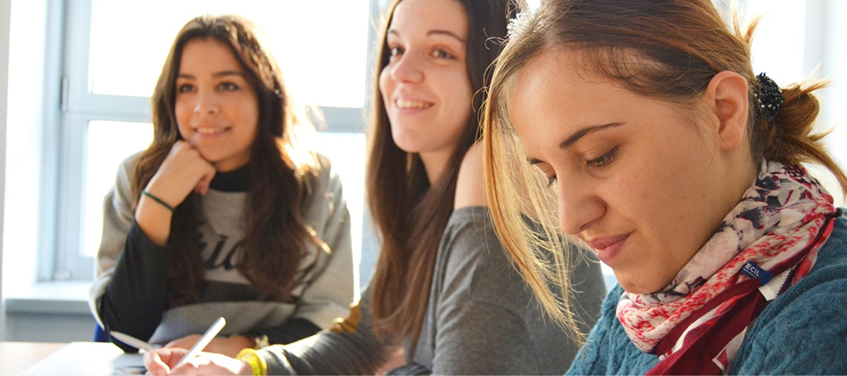 A table scene featuring three young women, one of whom is smiling brightly.