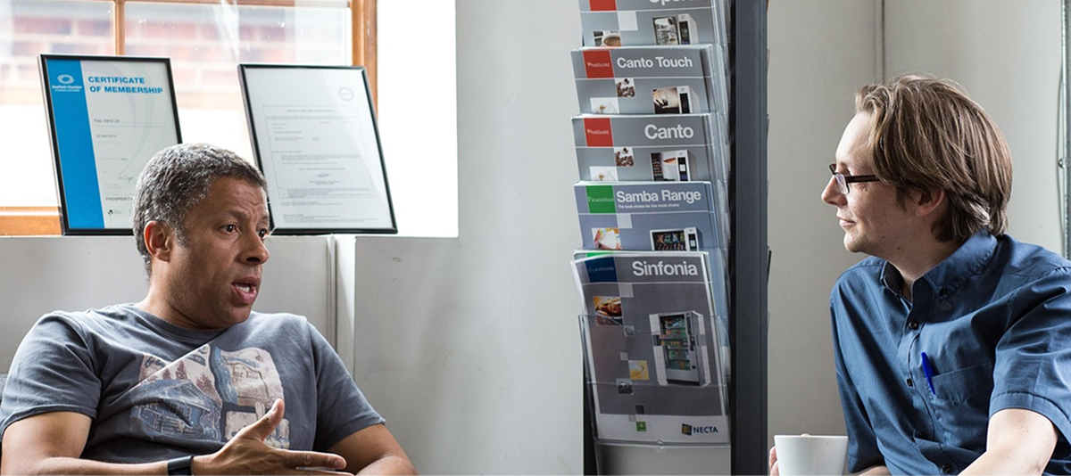 Two men engaged in conversation while seated at a table, sharing ideas and expressions.