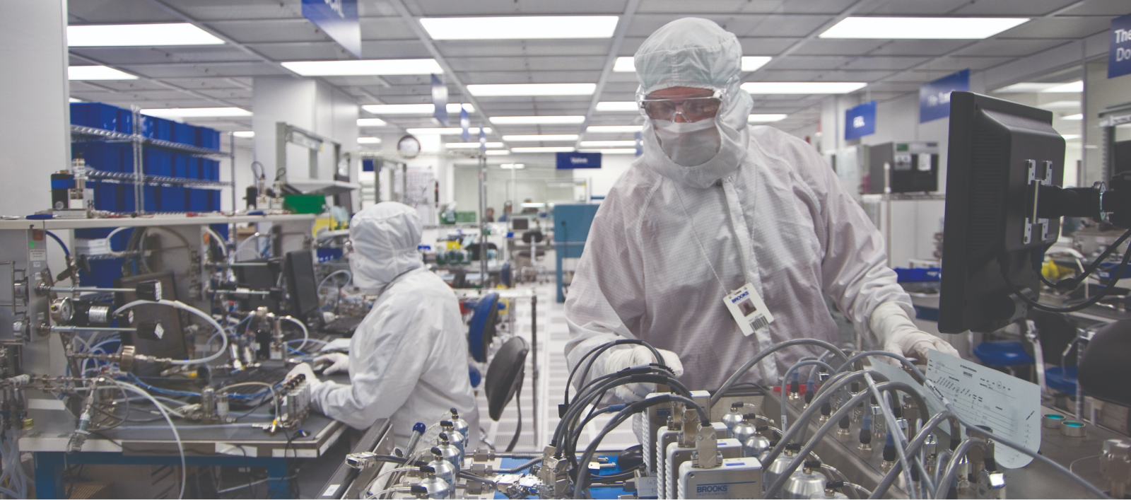 在一间现代化的无尘室里，两名身着白色西装的人正在合作研究布鲁克斯仪器。