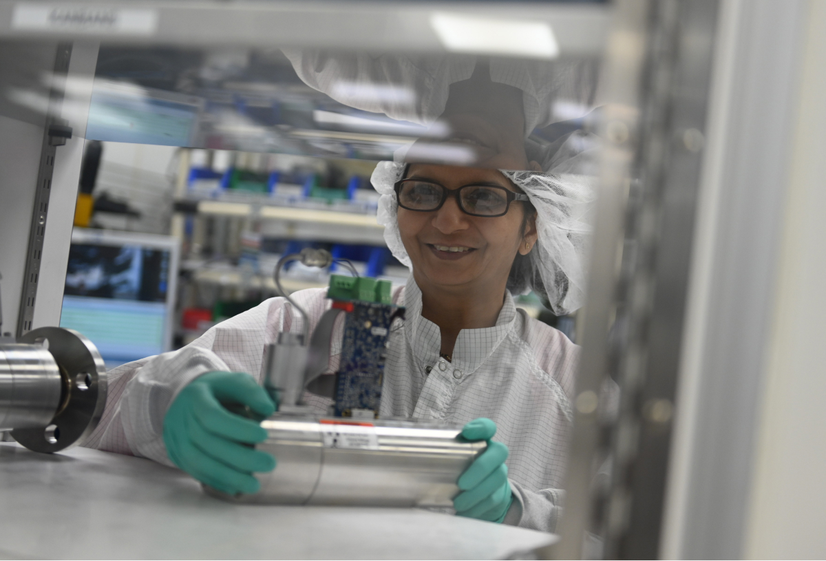 A woman in a lab coat and gloves holds a scientific device, focused on her work in a laboratory setting.
